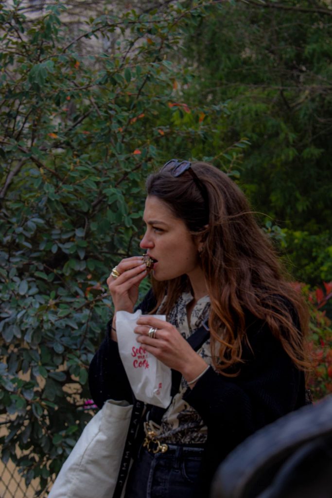 femme cheveux bouclés aux vent, mangeant un cookies dans un parc